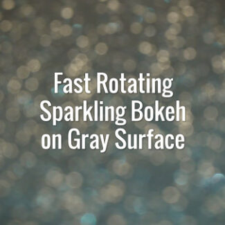 Seamlessly looping spinning flickering light yellow bokeh particles on gray surface.